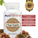 Haritaki Tablets bottle with haritaki fruit and powder on white background, AyuMantra dietary supplement.